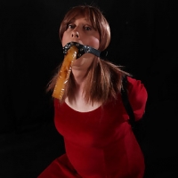 Luci May is dressed in a lucious red dressed & as about to be gagged.